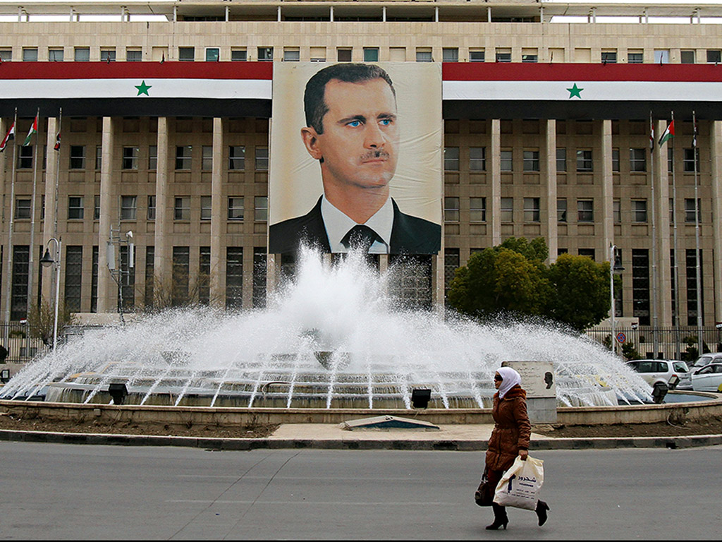 A woman walks past the central bank building decorated with a huge banner of President Bashar al-Assad in Damascus