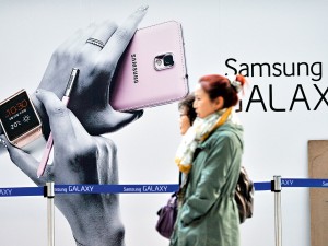 Pedestrians walk past a sign advertising Samsung Electronics’ Galaxy Note 3 smartphone at a railway station in Seoul