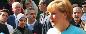 Refugees look on as German Chancellor Angela Merkel speaks to the media after she visited the AWO Refugium Askanierring shelter for refugees in Berlin, Germany