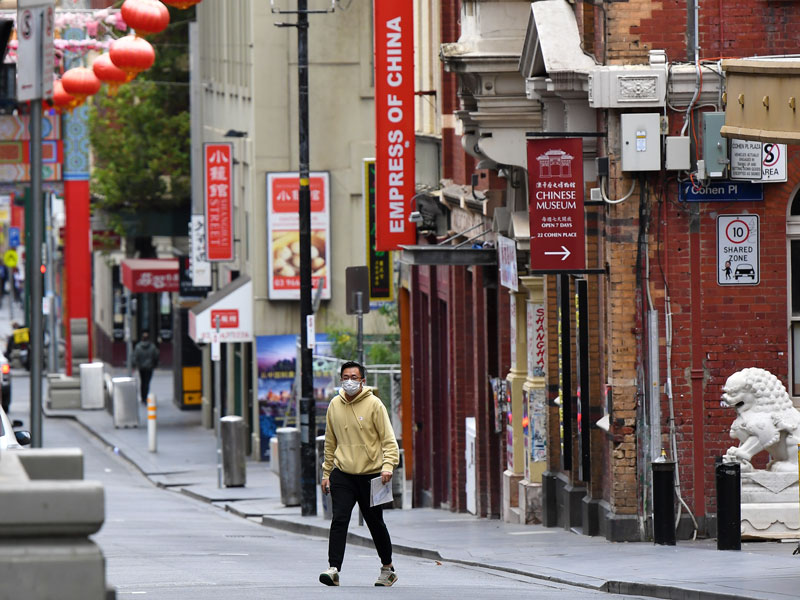 A man wearing a face mask crosses the road in China Town in Melbourne, Australia